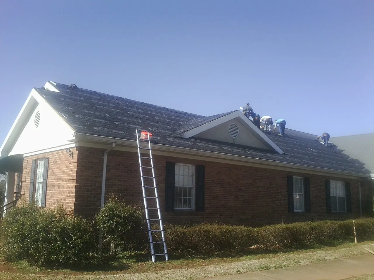 Crew tearing shingles off a brick ranch roof with a ladder set — Emergency Roof Repair work by our crew in Flandreau