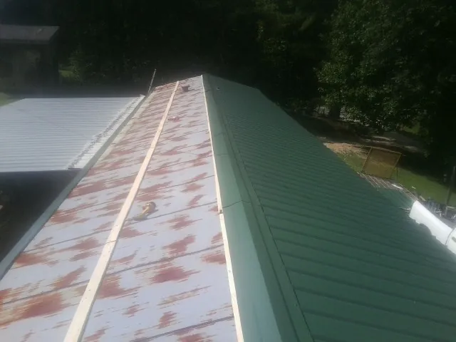 Old rusted panels beside newly installed green metal roofing — Wind Damage Roof Repair by Roofing Brothers in Flandreau