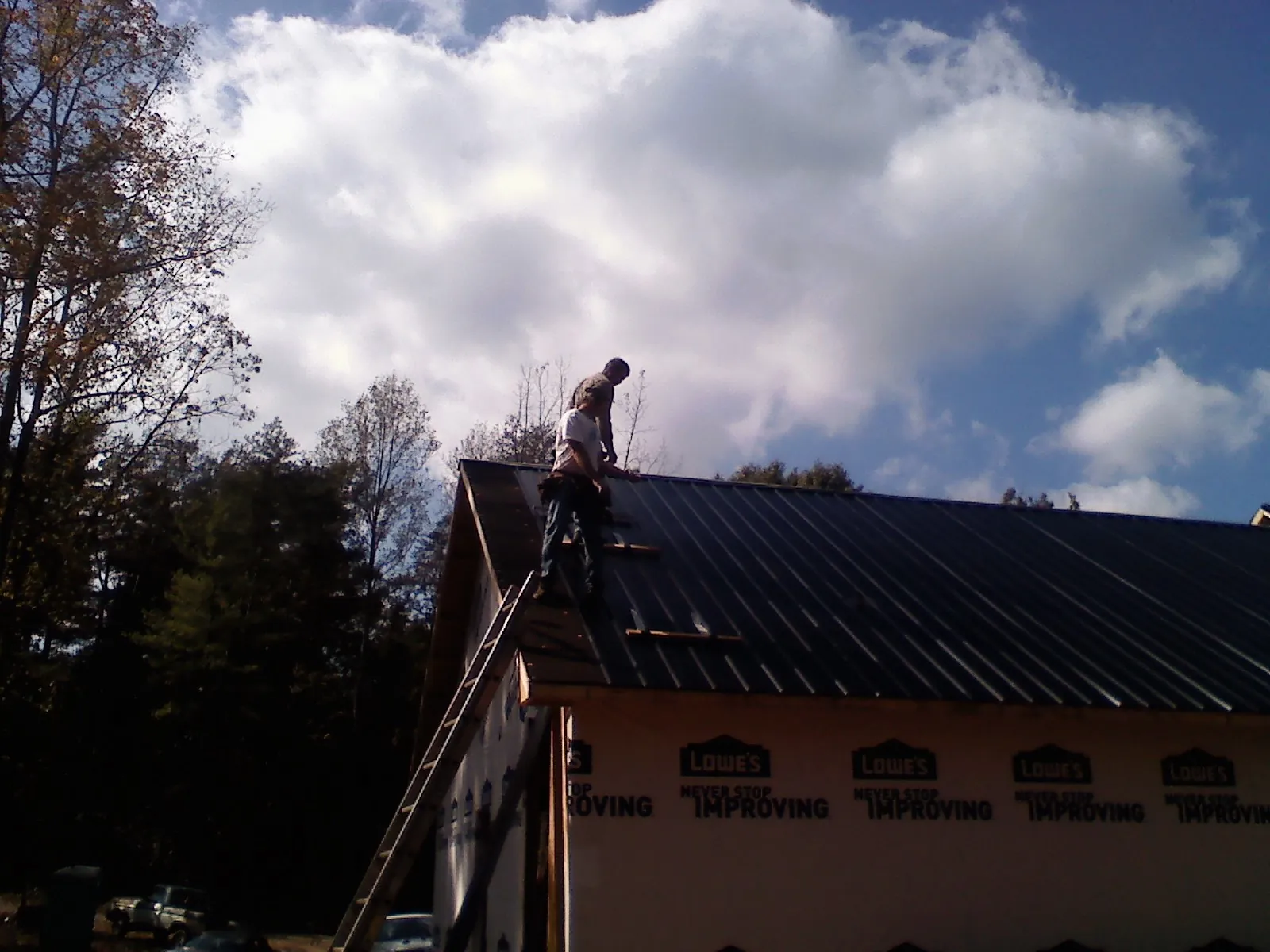Roofer fastening dark metal panels high against a cloudy sky, from a Roof Inspection job in Flandreau