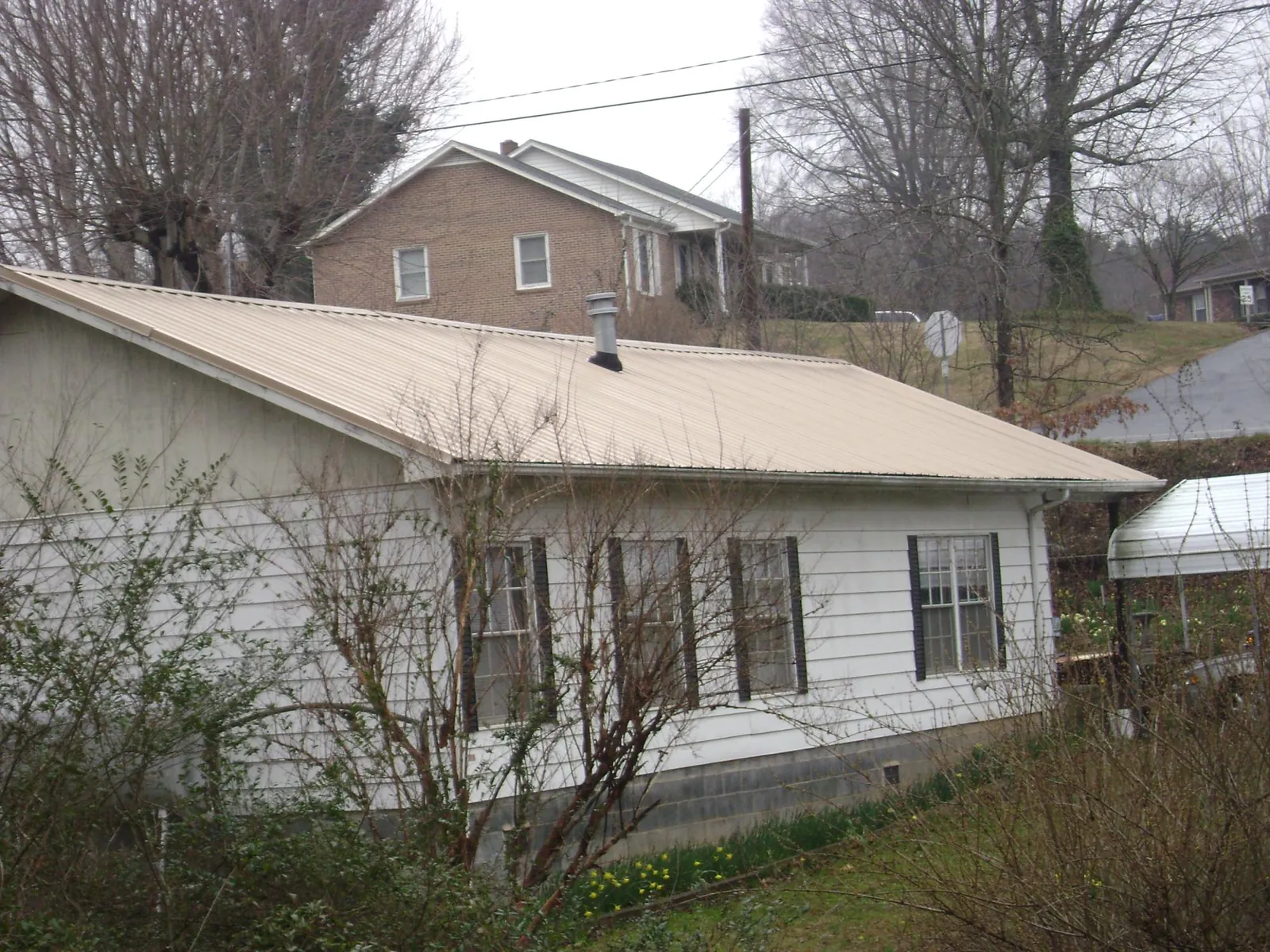 Tan metal roof on a white sided house set into a hillside — Commercial Roofing by Roofing Brothers in Flandreau